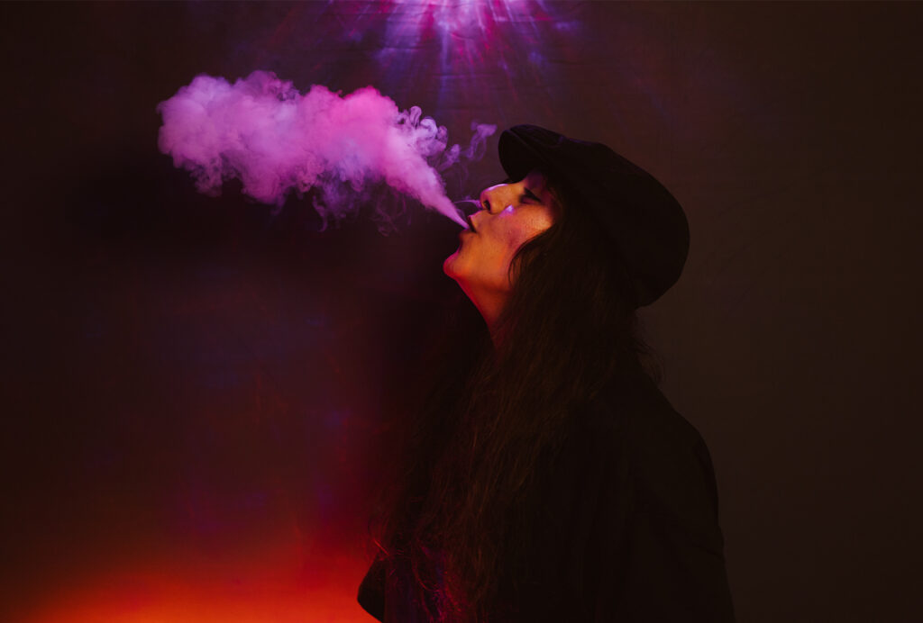Musikerin Leyla Mei Parker atmet Rauch aus unter lila Lichteffekten. 